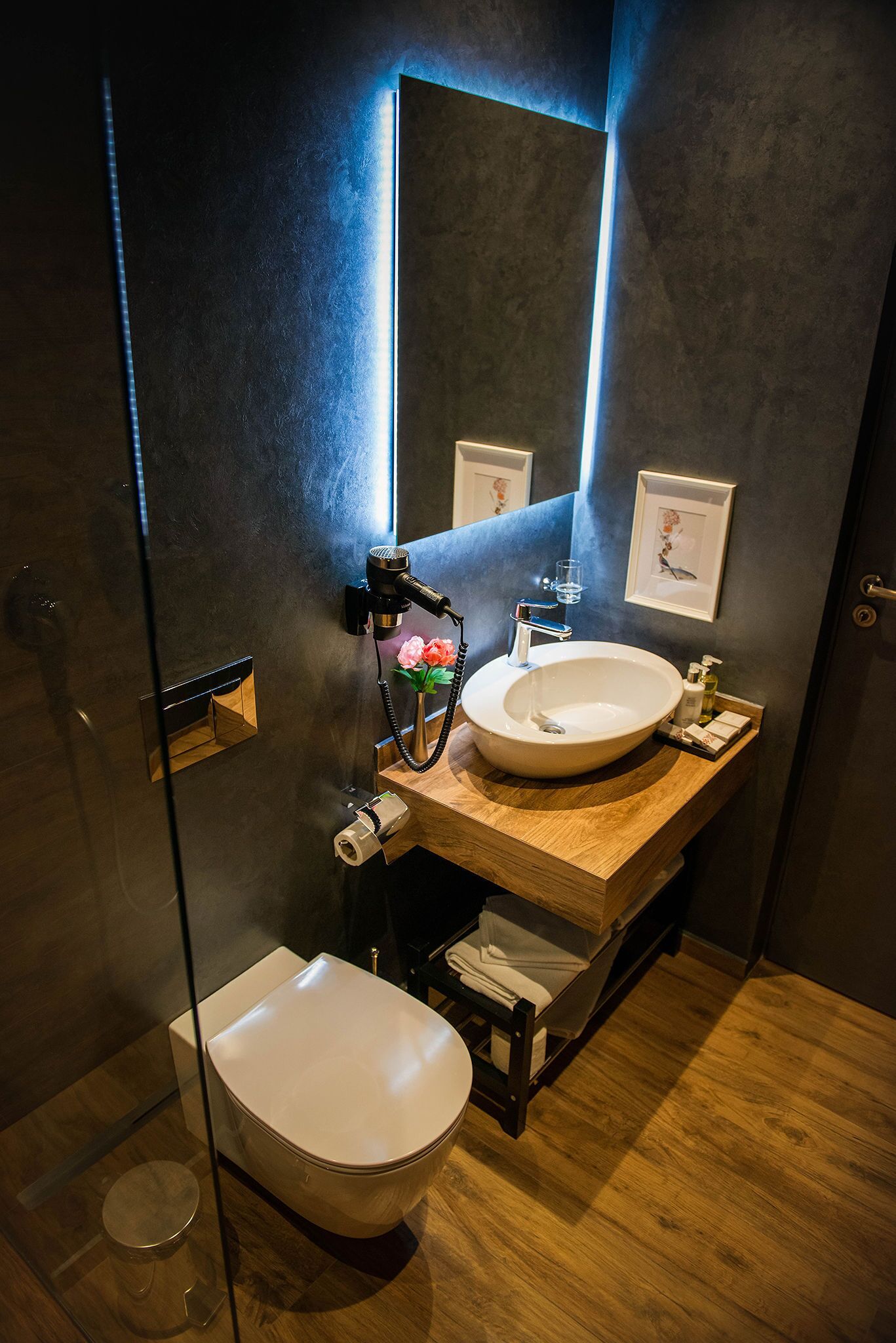 Un baño moderno con cabina de ducha de vidrio, tocador de madera con lavamanos blanco y un espejo grande.