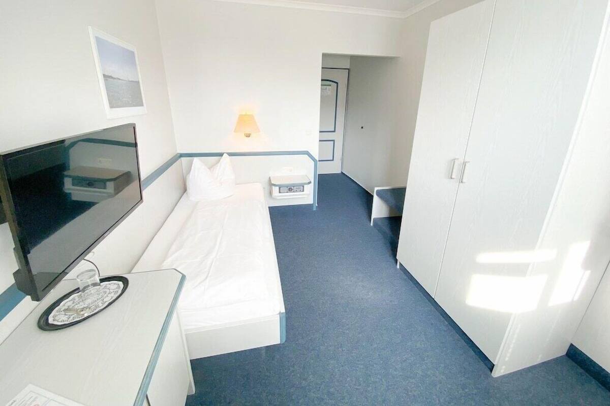 A hotel room with a bed, a desk with a flat-screen TV, a lamp, and a wardrobe.