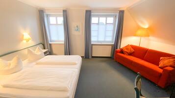 Et hotelværelse med en seng, en rød sofa, to vinduer med gardiner, en radiator og en vægmonteret lampe.