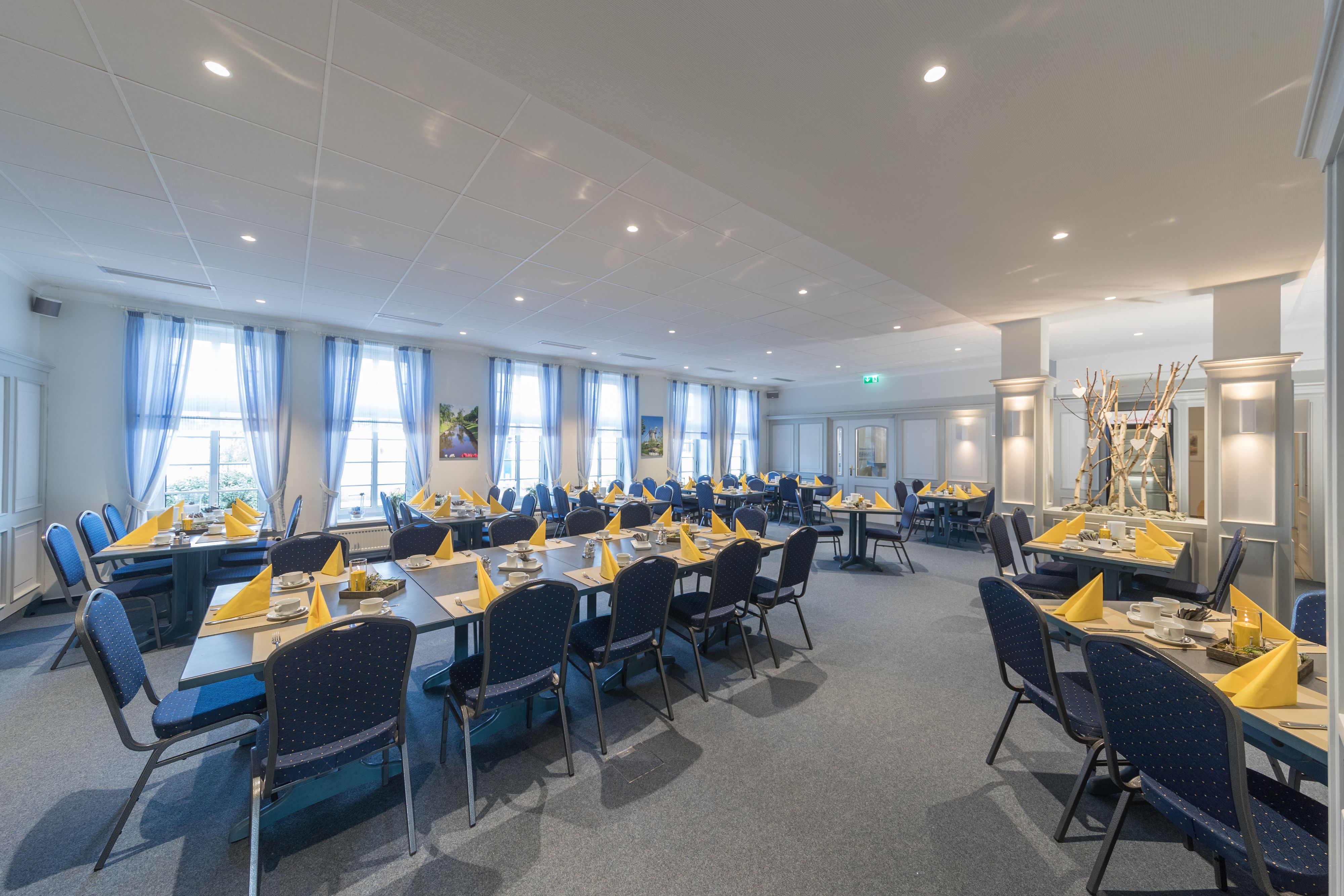 A large conference room with multiple tables and chairs, arranged in rows.