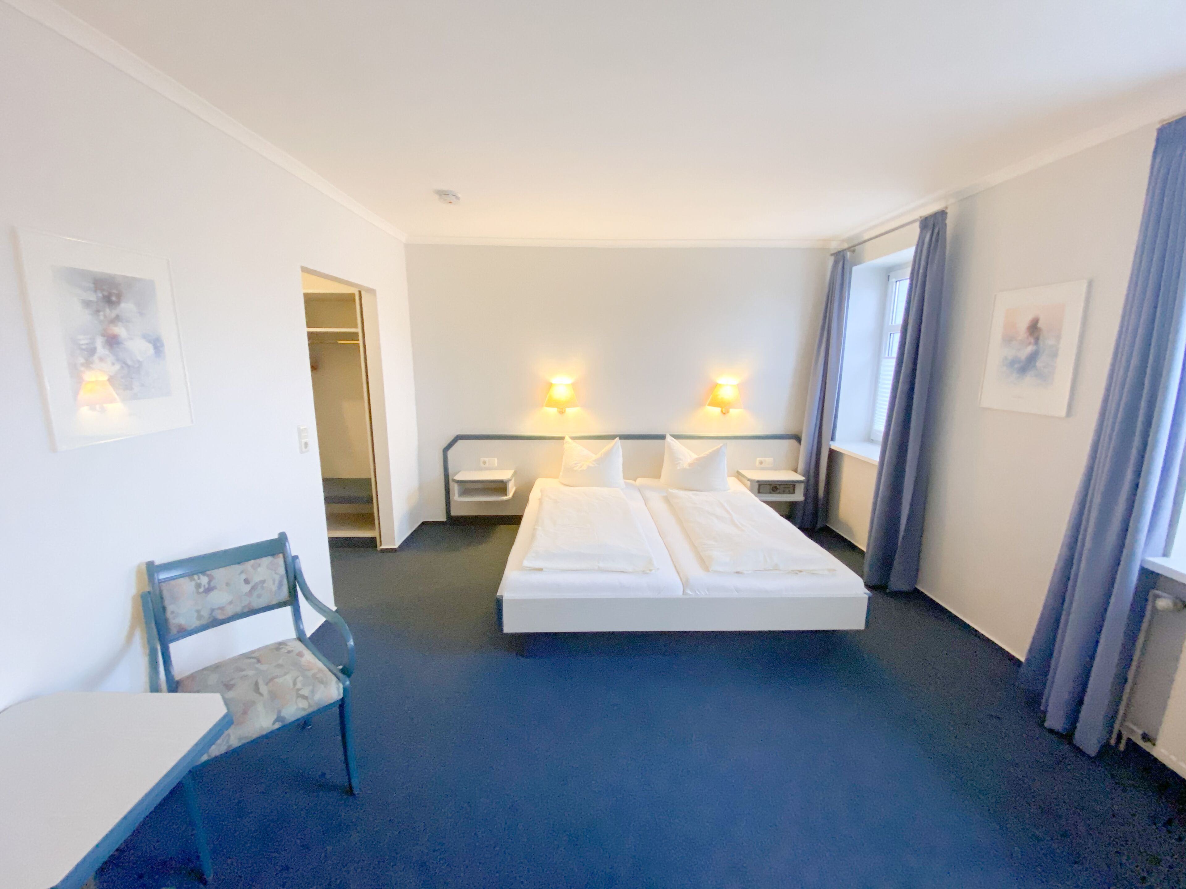 A hotel room with a large bed, bedside tables, a chair, and a desk.