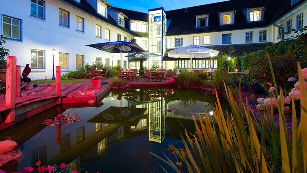 A courtyard with a pond, outdoor seating, and a restaurant named "Fleischauer Pilsner". - Hotel Wikingerhof (Kropp)