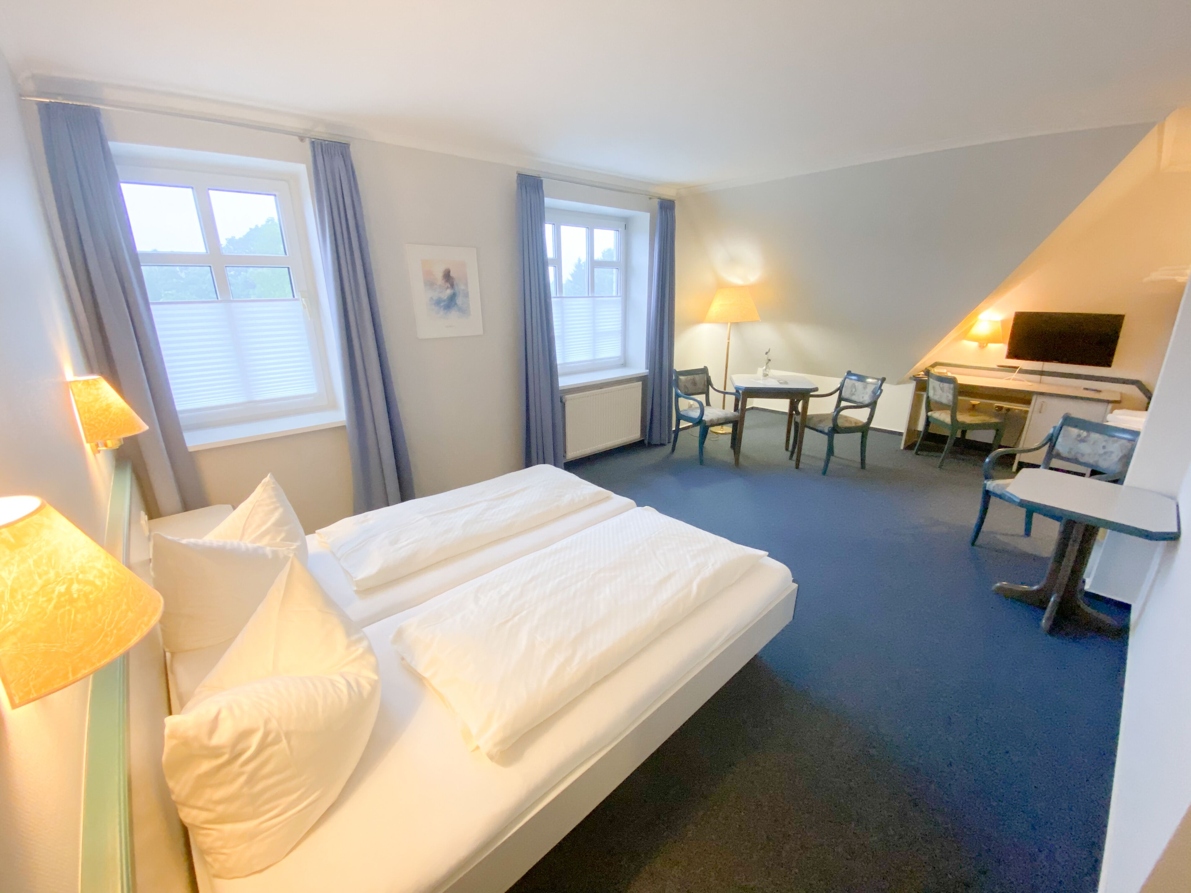 A hotel room with a bed, two bedside tables, a desk with a chair, a lamp, and a TV.