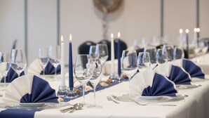 A table set for a formal dining event with white tablecloths, blue napkins, and clear glassware. - Hotel Wikingerhof (Kropp)