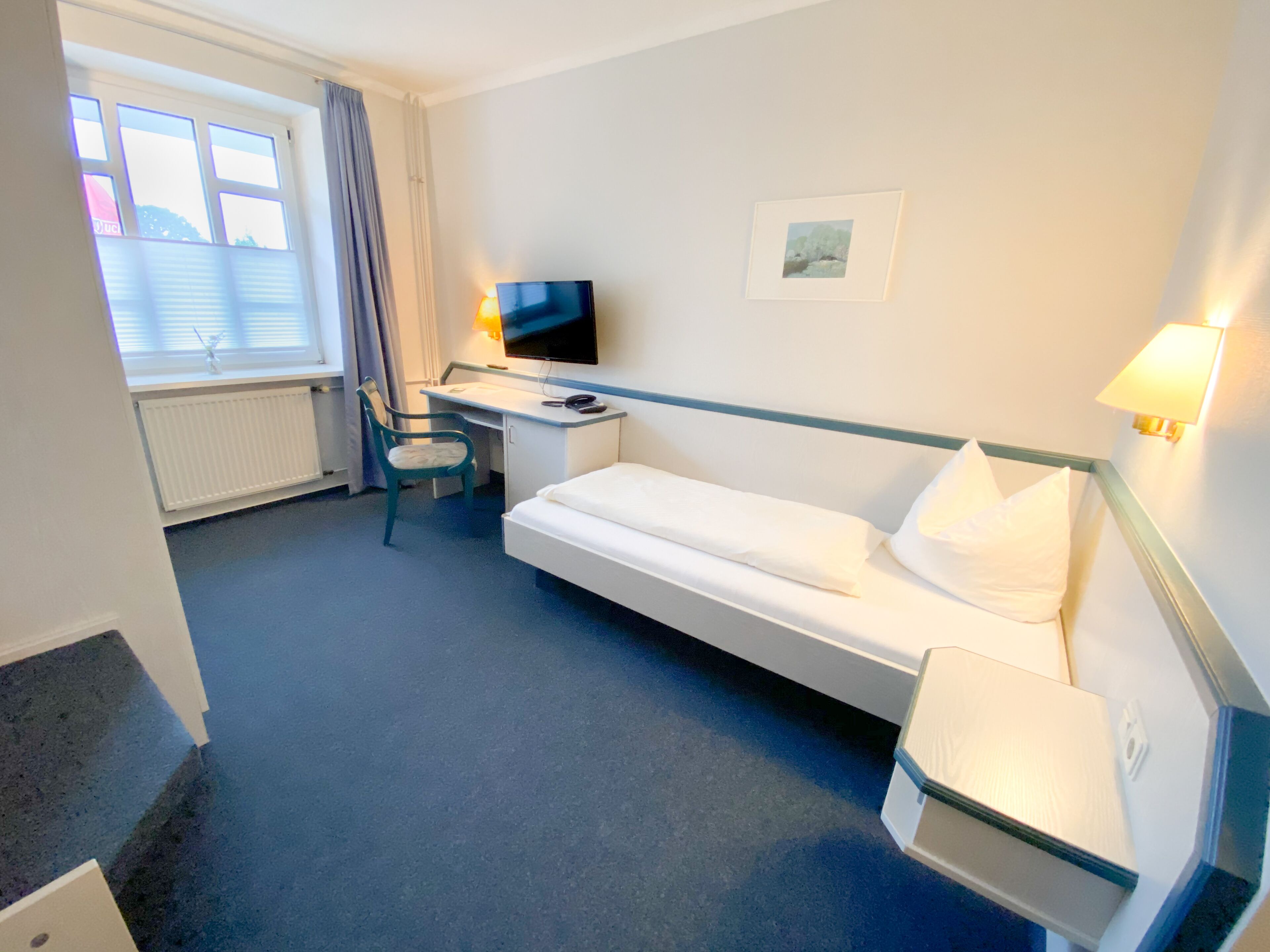 Habitación de hotel con cama, escritorio, silla, televisor y ventana con cortinas.