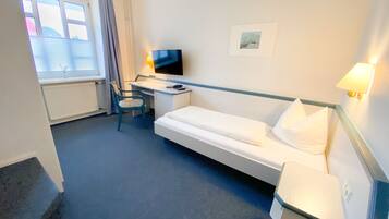 Habitación de hotel con cama, escritorio, silla, televisor y ventana con cortinas.