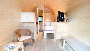 A cozy, wooden cabin-style room with a bed, a wicker chair, a small table, and a television. - Hotel Wikingerhof (Kropp)