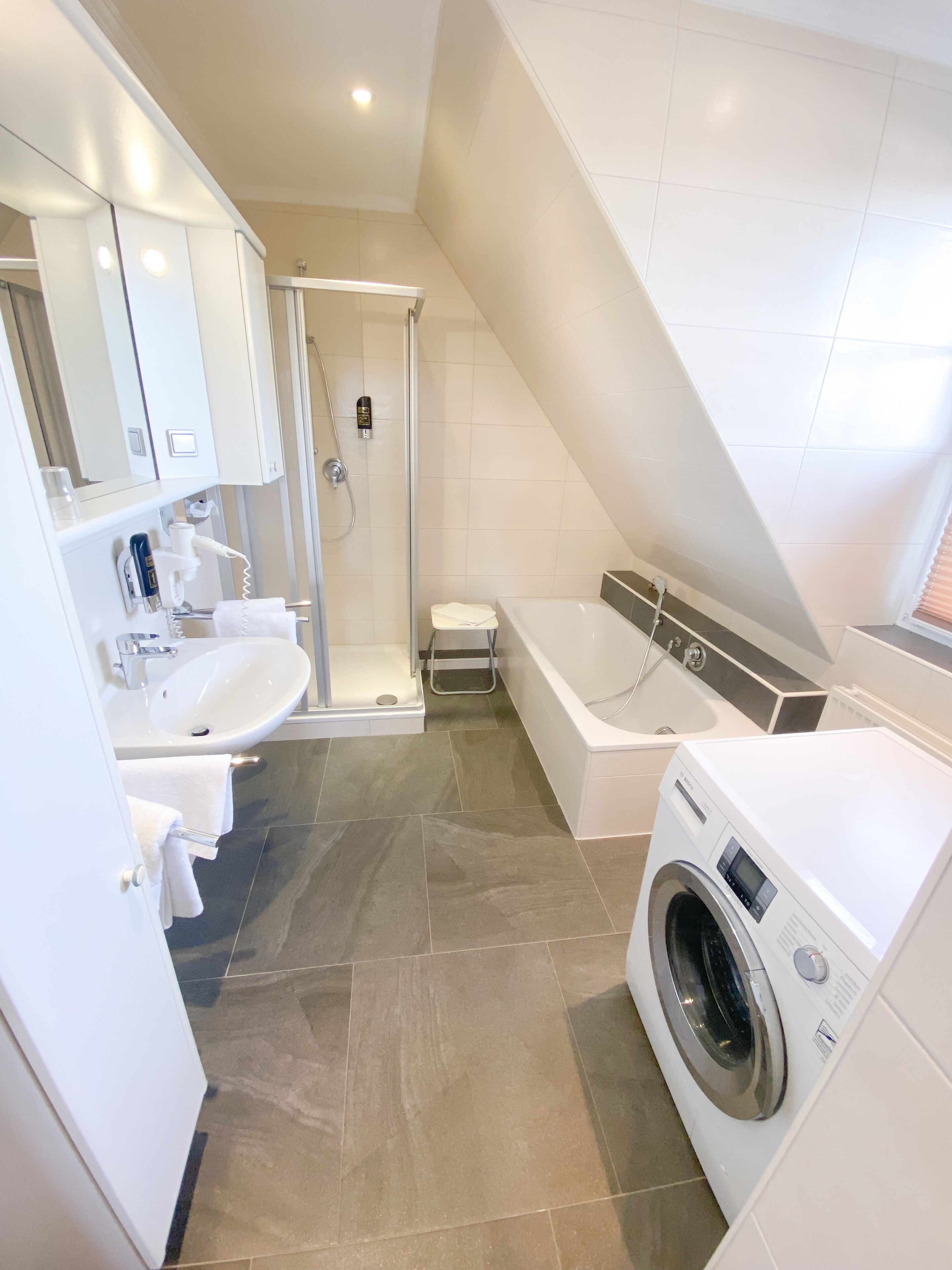 A modern bathroom with a shower, sink, and washing machine.