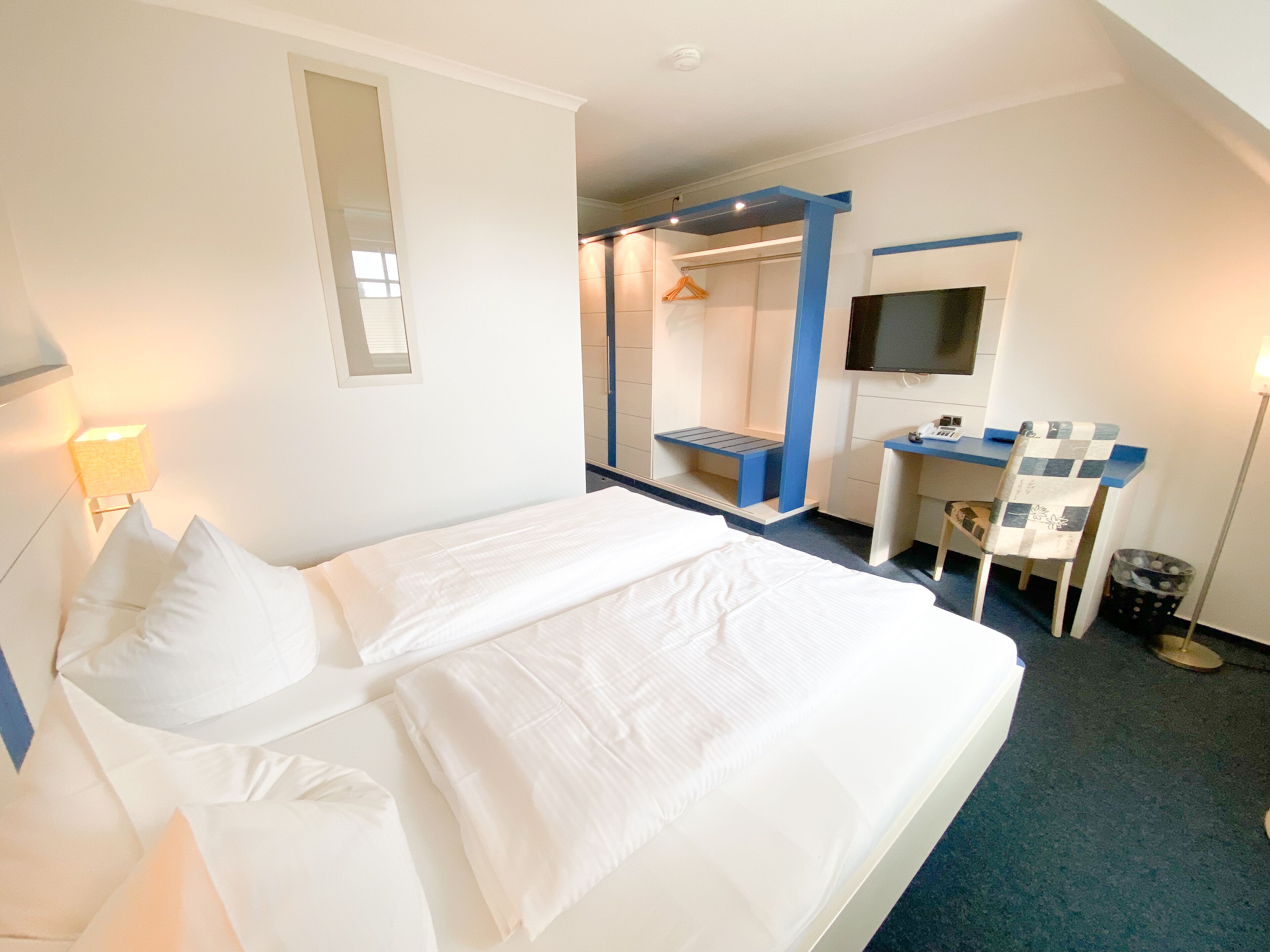 A hotel room with a bed, a desk, a chair, a TV, and a wardrobe.