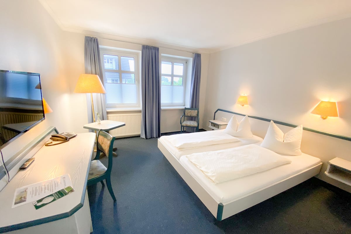 A hotel room with a bed, desk, chair, and a TV.
