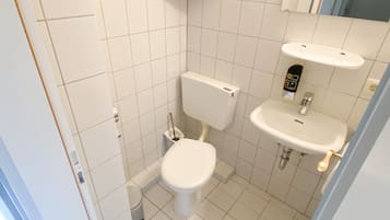 Ein kleines, sauberes Badezimmer mit weißen Fliesen, Toilette, Waschbecken und Spiegel.