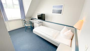 A hotel room with a single bed, a desk with a chair, a television, and a window with curtains.