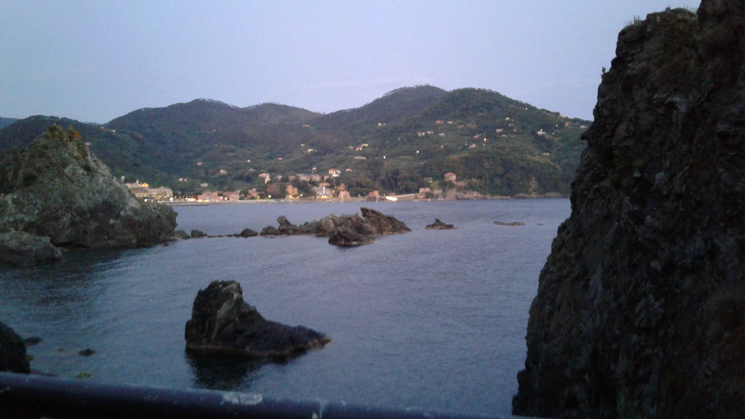 A coastal landscape with rocky outcrops and a distant town on the hills.
