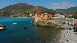 A coastal town with boats docked near a rocky shore, a small building, and mountains in the background. - Zulin Farm. Air-conditioned accommodations for 4–7 people 011017-AGR-0025 (Levanto)