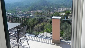 A balcony with a table and chairs, overlooking a mountainous landscape with buildings in the distance. - Zulin Farm. Air-conditioned accommodations for 4–7 people 011017-AGR-0025 (Levanto)
