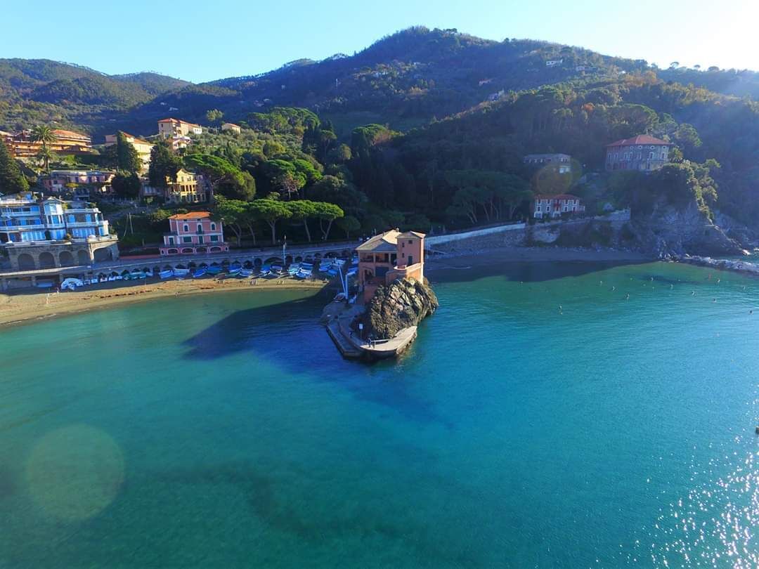 Un pueblo costero con un edificio destacado sobre un promontorio rocoso, rodeado de aguas azules y cristalinas.