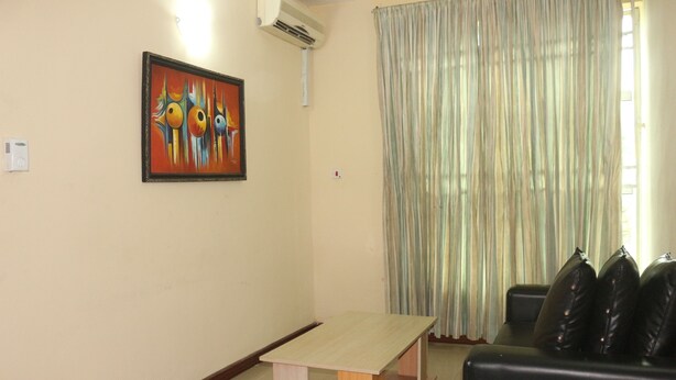 Una habitación con una mesa de madera, un sofá de cuero negro, un cuadro en la pared y una ventana con cortinas.