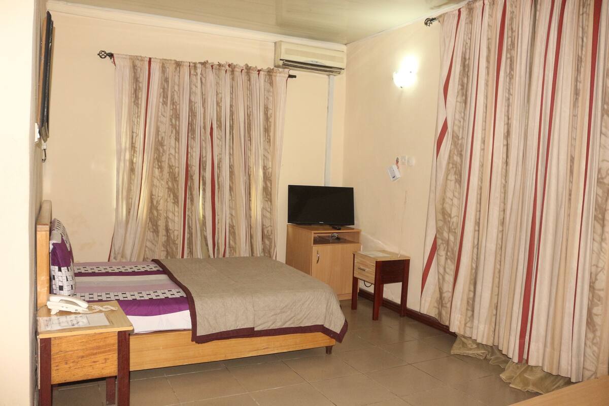 A bedroom with a bed, a television, a desk, and a chair.