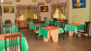 Un comedor con varias mesas y sillas, unidades de aire acondicionado y elementos decorativos como cortinas y cuadros.