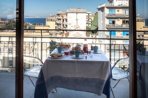 A balcony with a table set for breakfast, overlooking a coastal cityscape. - AMORE RENTALS - Apartament Erica with Private Terrace, Air Conditioning and WI-FI near piazza Tasso (Sorrento)