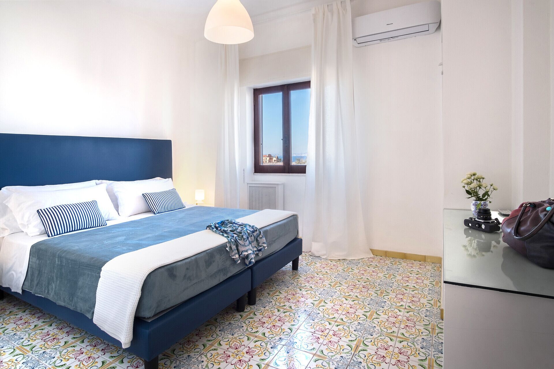 Une chambre d’hôtel avec un lit, une fenêtre avec des rideaux, un radiateur et un sol carrelé.