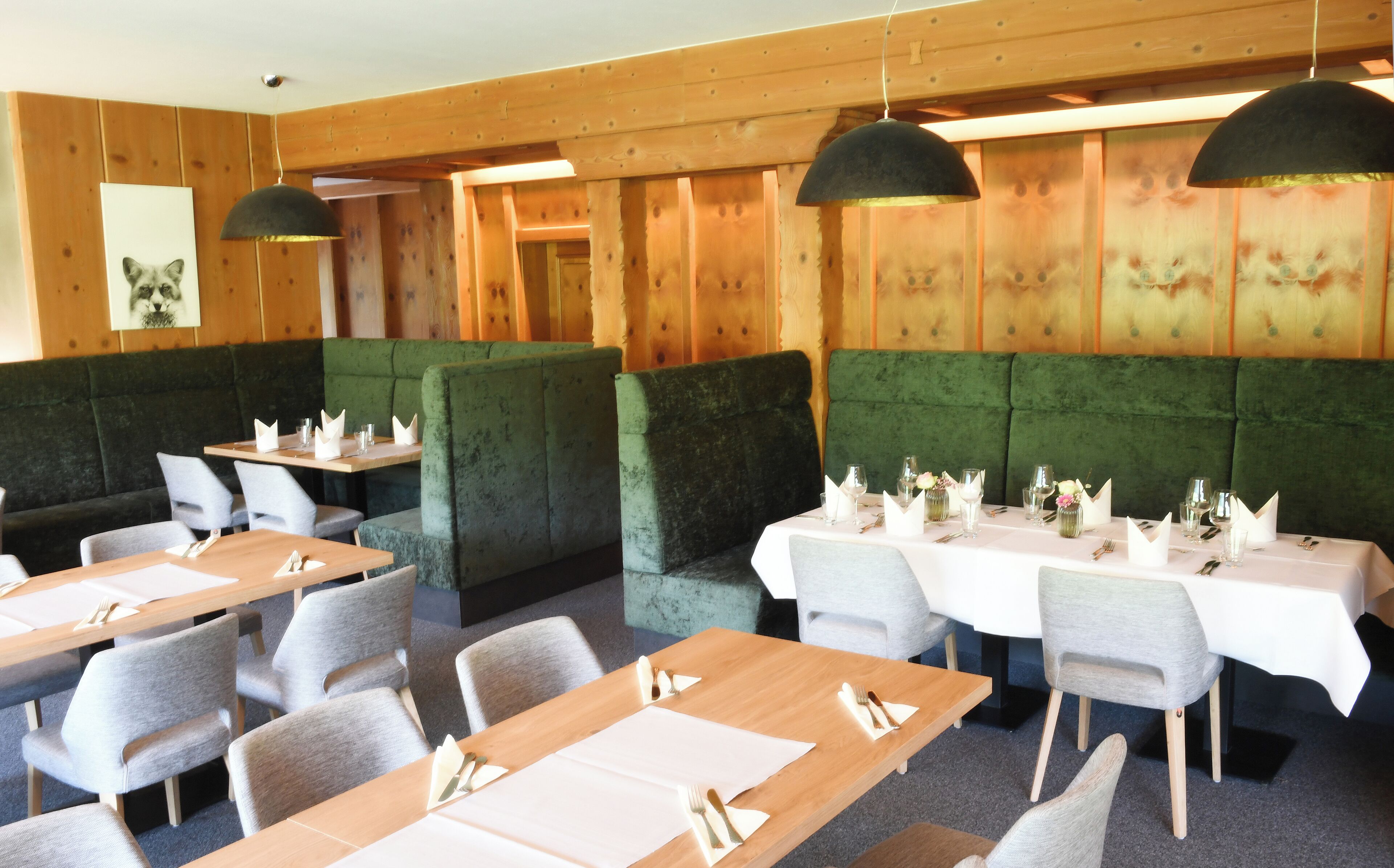 Un restaurante con paredes de paneles de madera, asientos tapizados en verde y mesas dispuestas con manteles blancos y cubiertos.