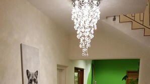 A hallway with a chandelier, a framed artwork of a fox, a patterned rug, and a reception desk with a green backdrop. - Fuxxbau Fischerbach (Fischerbach)