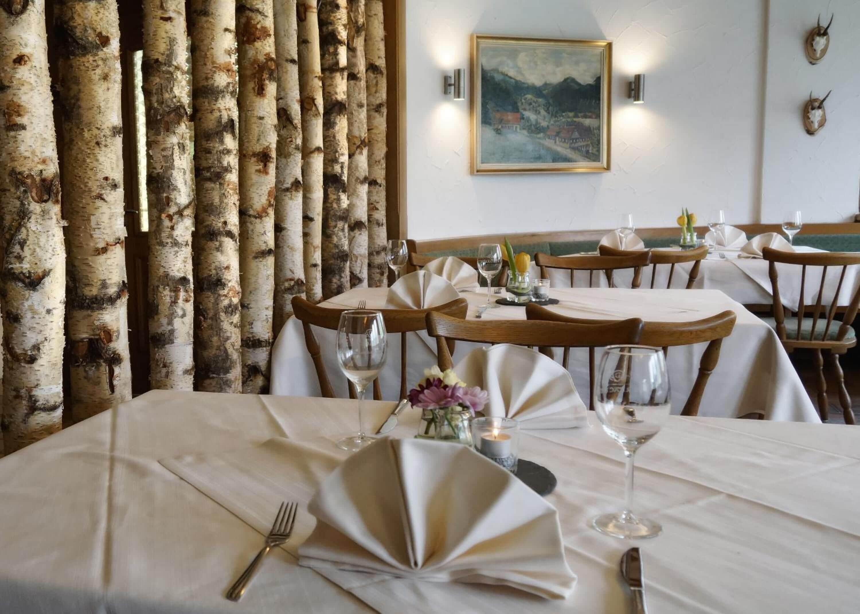 A restaurant with birch tree decor, white tablecloths, and a painting on the wall.