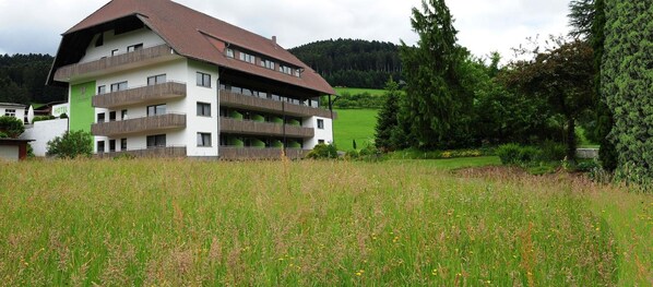Un hotel de varios pisos con balcones, rodeado de un campo cubierto de césped y árboles.