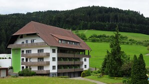 A multi-story hotel with balconies, surrounded by a lush green landscape and forested hills. - Fuxxbau Fischerbach (Fischerbach)