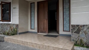 Una entrada de edificio con puerta de madera, pared de piedra y porche con baldosas.