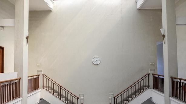 Un interior espacioso con techo alto, un reloj central y una escalera con barandillas de madera.