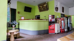 A reception area with a green counter, a television mounted on the wall, a Coca-Cola refrigerator, and a framed picture above the counter. - RedDoorz Plus near Jalan Baru Bogor (Bogor)