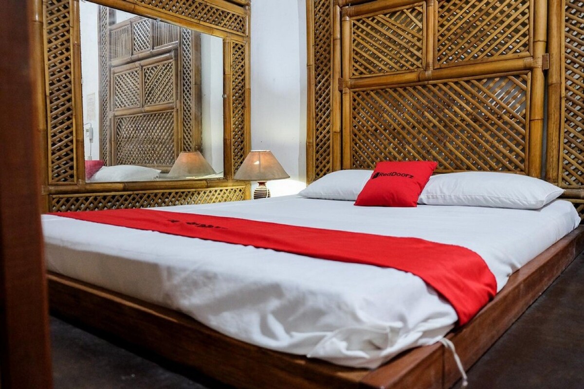 A bed with white and red bedding, a red pillow, and a wooden headboard.