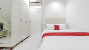 A hotel room with a bed, a wardrobe, a television on a stand, and an air conditioning unit.