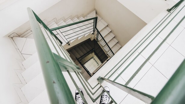 A view of a staircase with a green handrail and white steps, leading to a landing with a door.