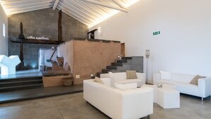 Een modern interieur met een trap, witte banken en een betonnen muur met een rustieke sculptuur.