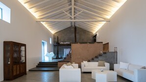 Een ruime woonkamer met een hoge plafond, witte banken, een houten kast en een trap naar een hoger gelegen verdieping.