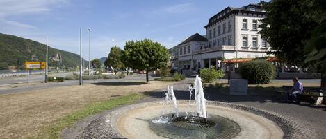 A public fountain with water jets in a circular basin, surrounded by cobblestone pavement. In the background, there is a multi-story building with a sign that reads "Hotel Zum Zorn."