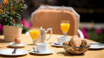 Une table mise pour le petit-déjeuner avec une carafe, deux verres de jus d’orange, un bol de pain et une plante en pot.