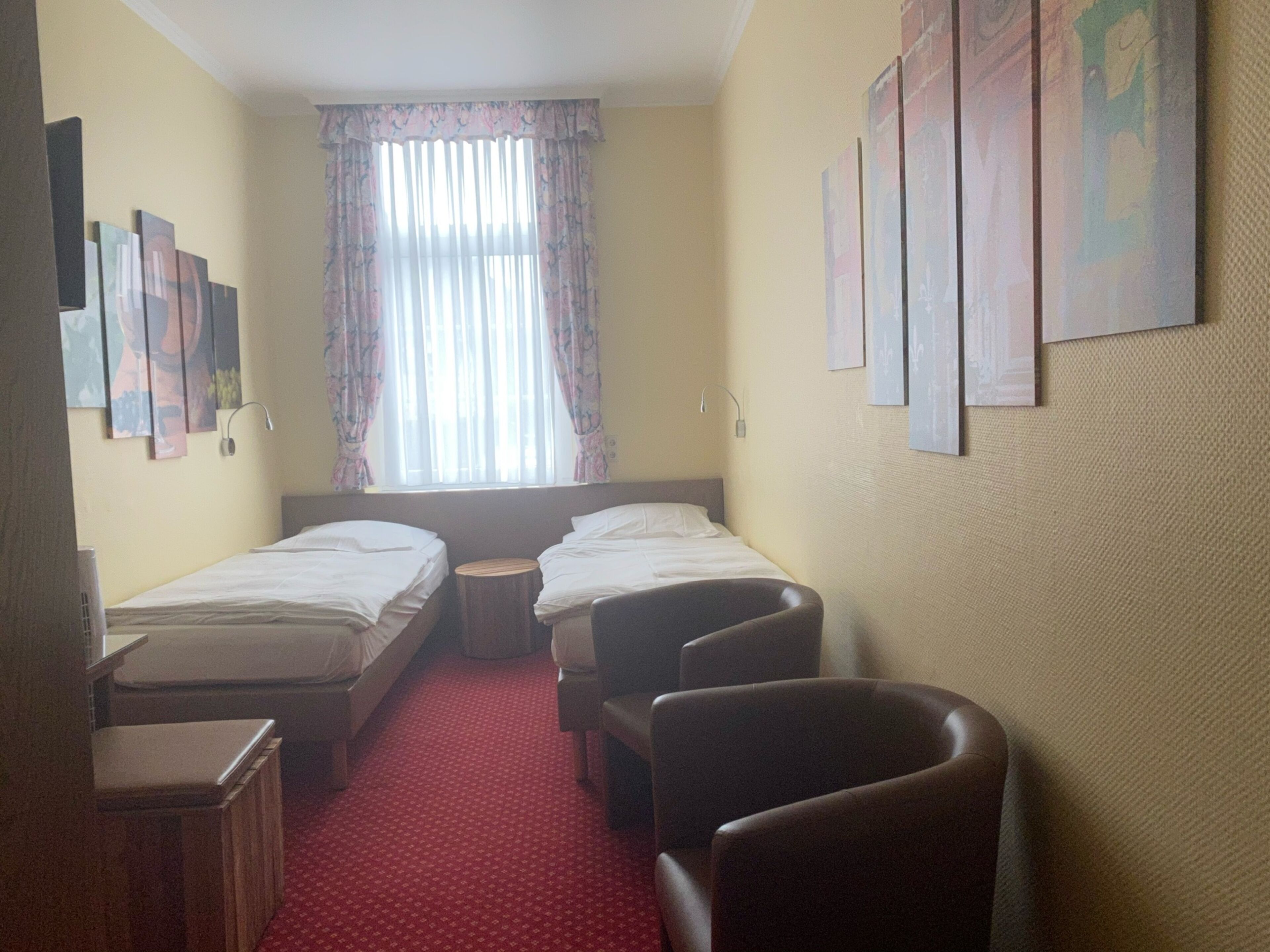 Hotellihuone, jossa on kaksi erillistä sänkyä, pieni puujakkara, työpöytä ja tuoli.