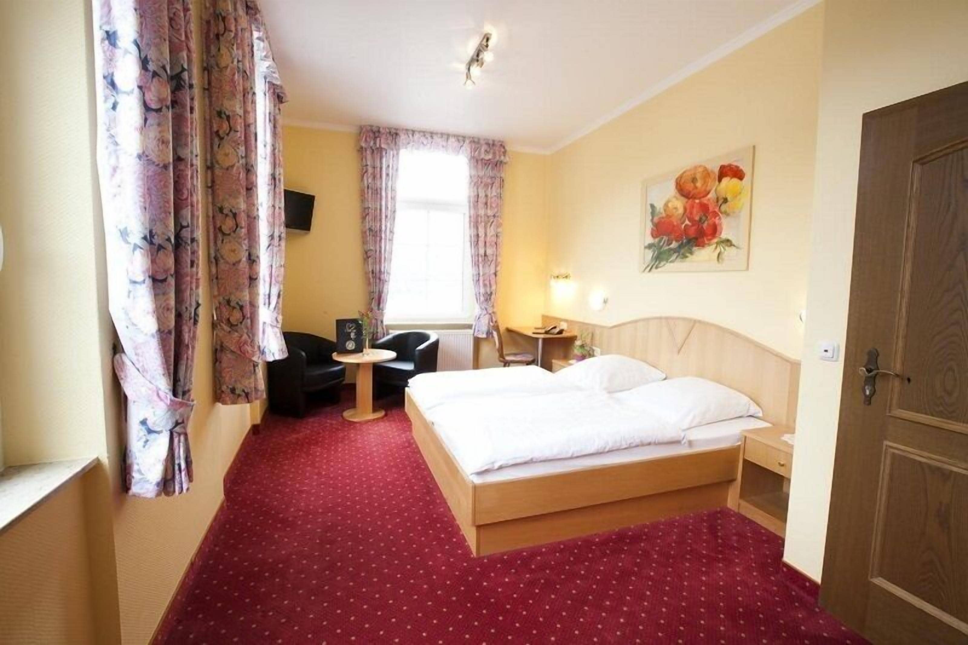 A hotel room with a bed, a desk, a chair, a TV, and a painting on the wall.