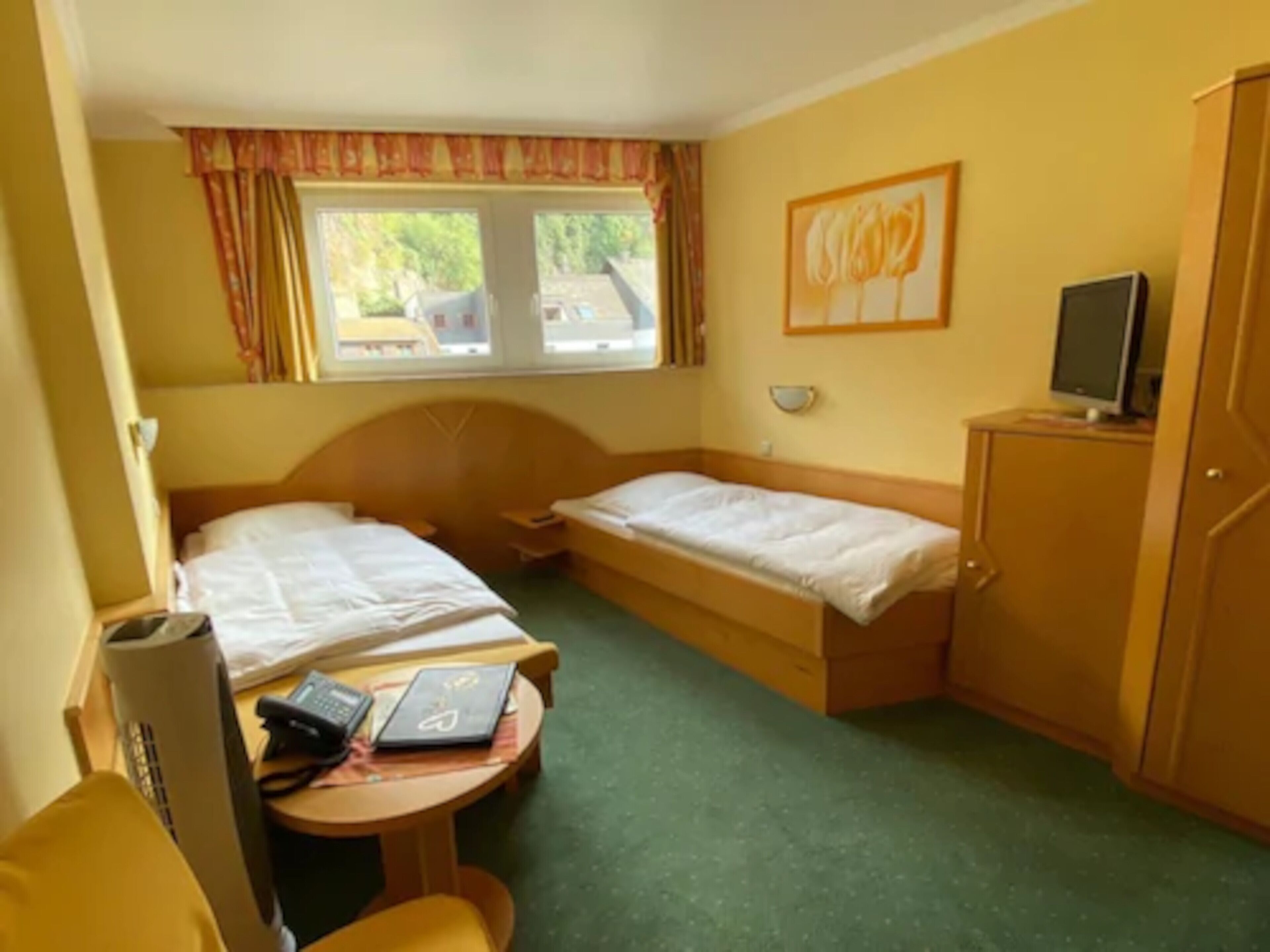 Ein Hotelzimmer mit zwei Einzelbetten, einem Schreibtisch mit Stuhl, einem kleinen Tisch, einem Fernseher und einem Kleiderschrank.