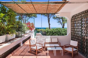 Une terrasse avec des meubles d’extérieur, une vue sur la mer et des plantes en pot.
