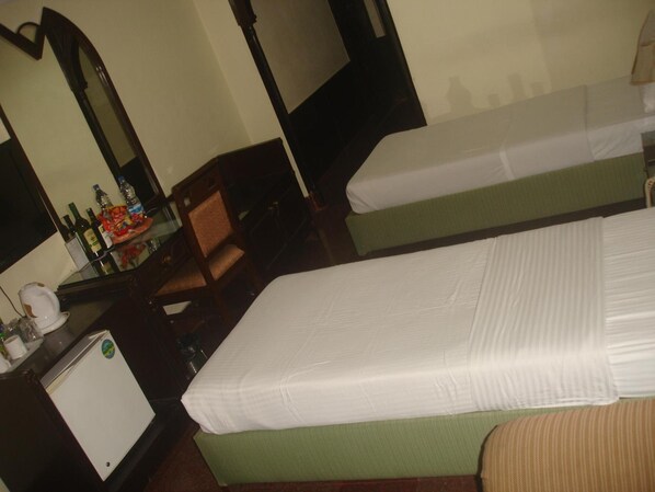 Habitación de hotel con dos camas individuales, un escritorio pequeño con espejo, una silla y un refrigerador.