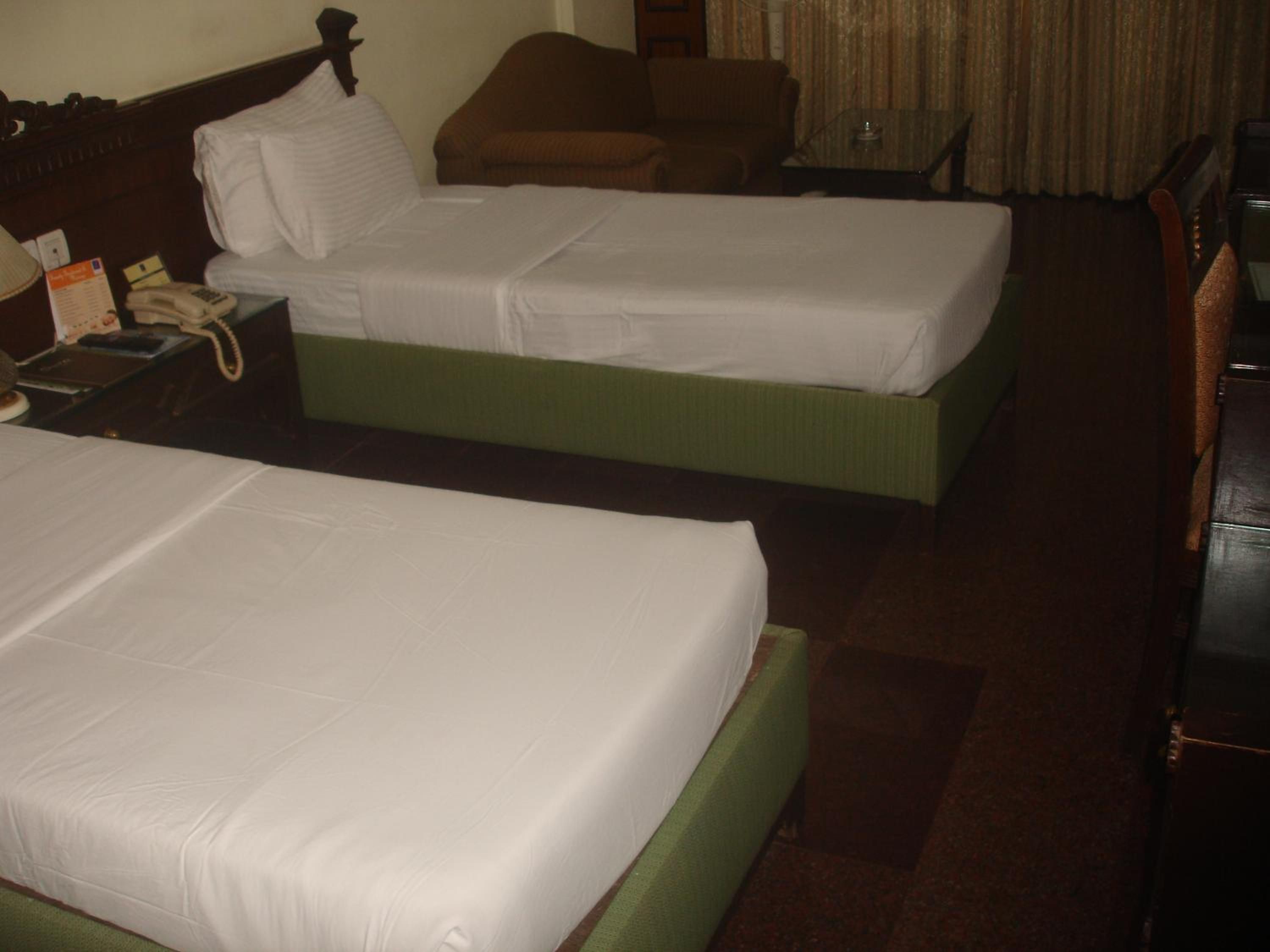 Habitación de hotel con dos camas individuales, una silla, una mesita y un teléfono.