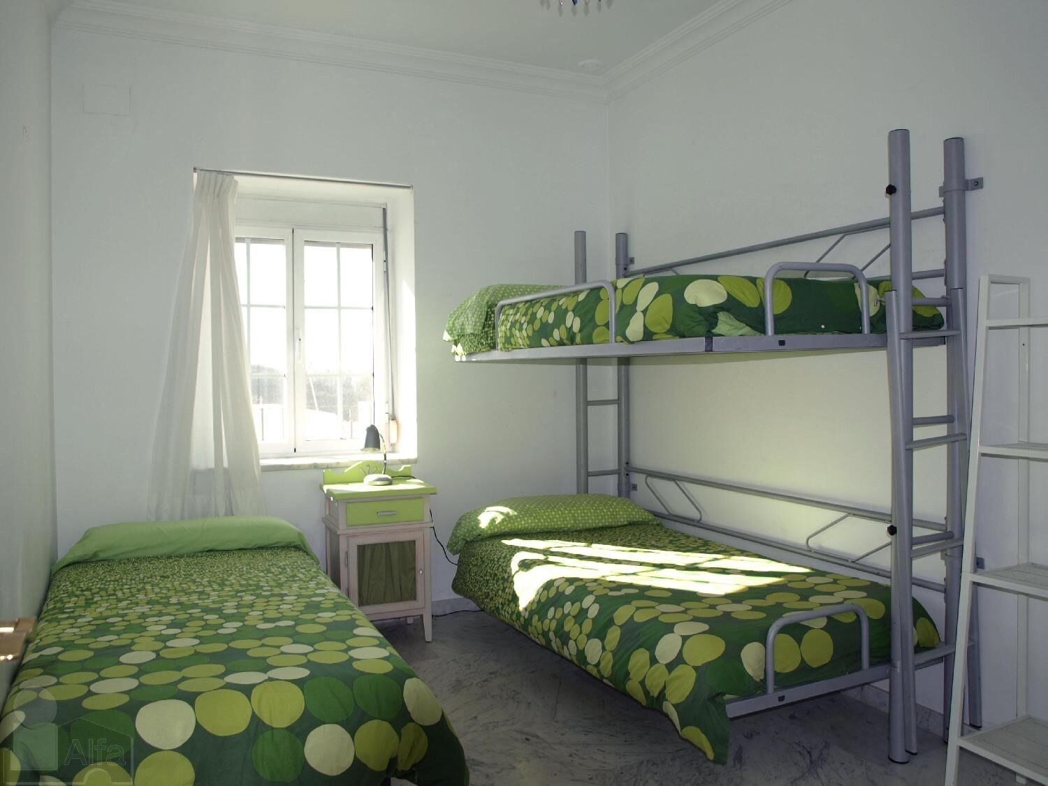 Habitación con literas, un escritorio pequeño y una cama con cubrecama verde de lunares.