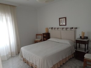 Un dormitorio con una cama grande, una mesita de noche, una silla y un cuadro enmarcado en la pared.