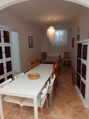 Un comedor con una mesa y sillas blancas, una lámpara colgante y un ventanal con cortinas.