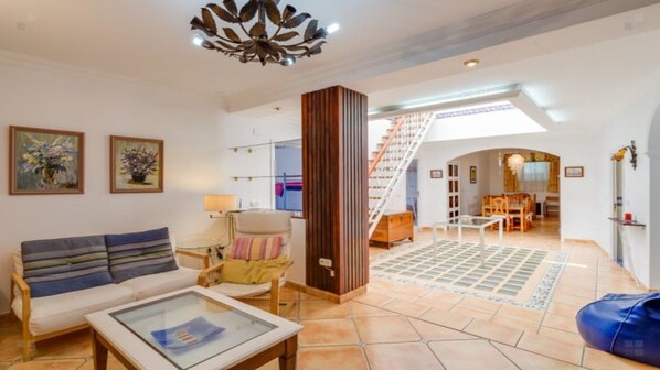 Amplia sala de estar con sofá, una mesa de centro y un columnario decorativo. Una escalera conduce a un nivel superior.